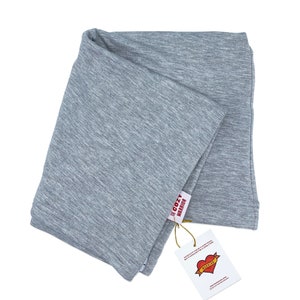May include: A gray, folded, soft, cotton scarf with a tag that says "The Cozy Warrior" and has a red heart with the word "Warrior" inside. The tag also says "Wear it proudly, be a cozy rebel, but it doesn't have to be a lonely one."