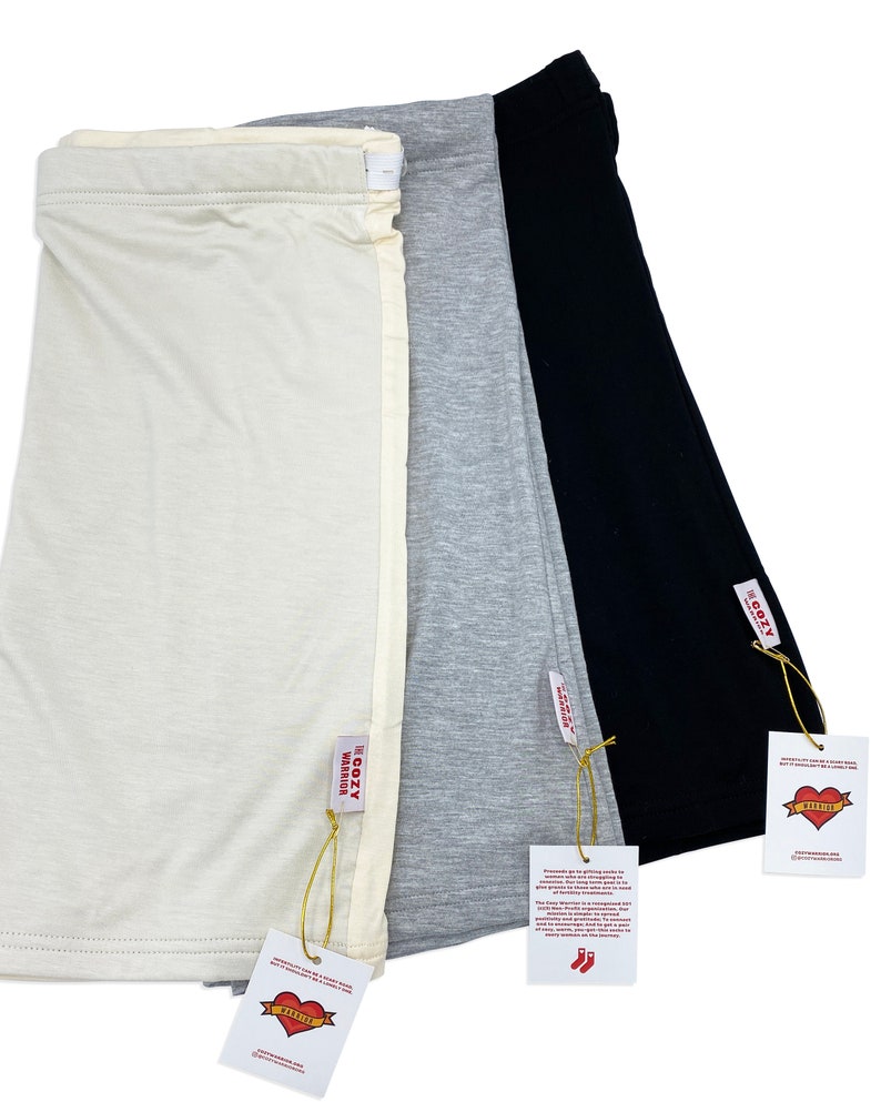May include: Three pairs of long, soft, stretchy, cotton leggings in ivory, gray, and black. Each pair has a tag that says "The Cozy Warrior" with a red heart logo.