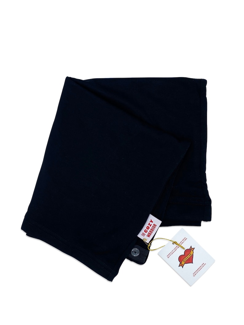 May include: A black, folded, cotton baby wrap with a white tag that says "The Cozy Warrior" and a red heart with the word "Warrior" inside.