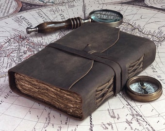 May include: A brown leather-bound journal with a compass and magnifying glass on a vintage world map. The journal has a braided leather strap and is closed.