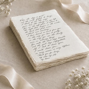 May include: A stack of off-white, rectangular paper sheets with rough, deckled edges. The top sheet features black cursive text that reads: When the day is quiet and the world forgets to hurry, I think of all the ways you've been the steady in my life.