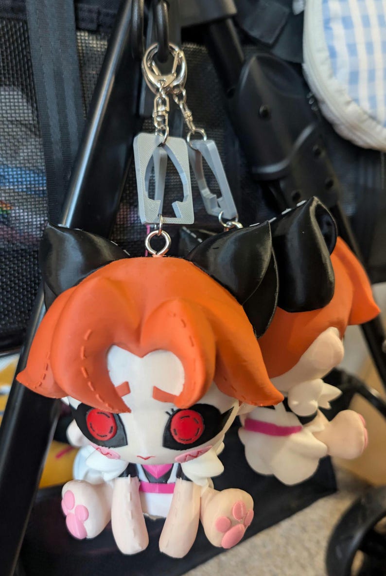 keychains featuring a cartoon character with orange hair, black ears, and red eyes. The character is wearing a white maid outfit with pink accents. The keychains are attached to a silver chain.
