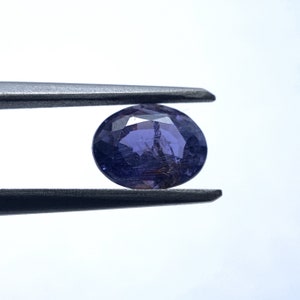 May include: A round, purple gemstone with a faceted cut. The gemstone is held in place by a pair of tweezers.