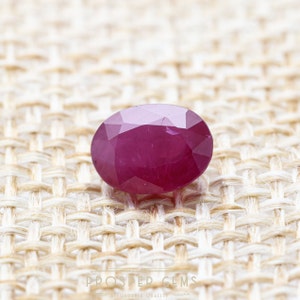 Op de afbeelding: Een levendige, ovale robijn edelsteen met een diepe rode tint. De edelsteen is gefacetteerd en heeft een gepolijste afwerking.