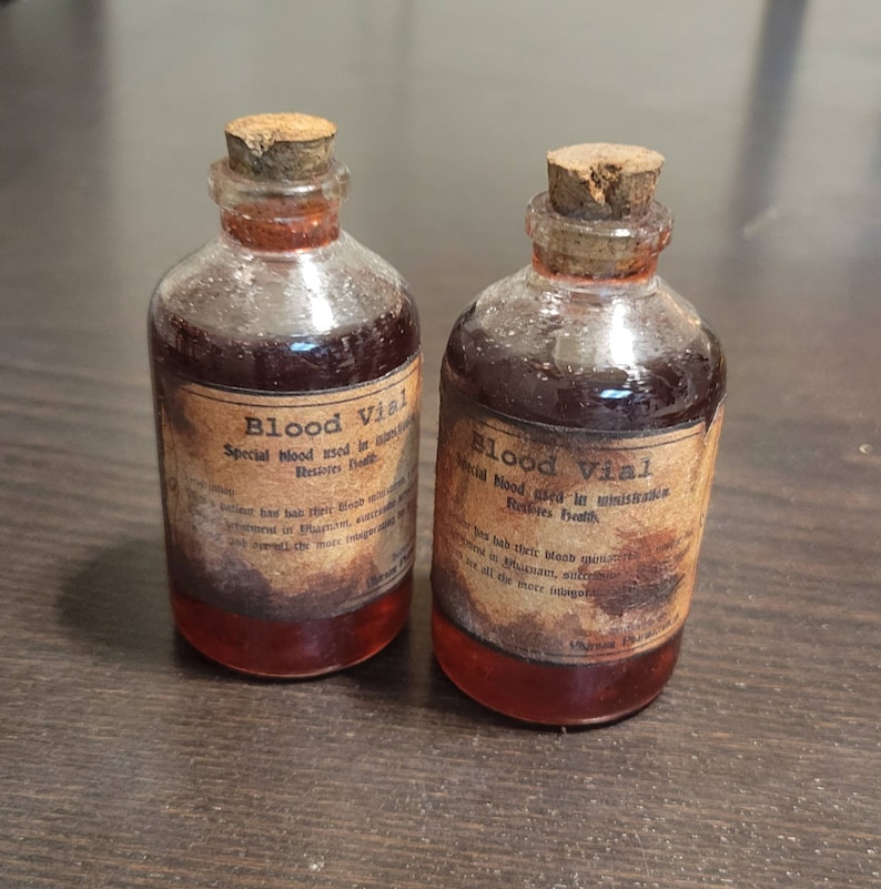 May include: Two small glass vials filled with a dark red liquid, each sealed with a cork stopper. The vials have aged, distressed labels that read "Blood Vial" and "Restores Health."