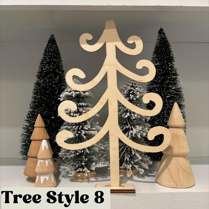 May include: A wooden Christmas tree cutout with a whimsical design. The tree is standing on a shelf with other smaller wooden trees and artificial pine trees.
