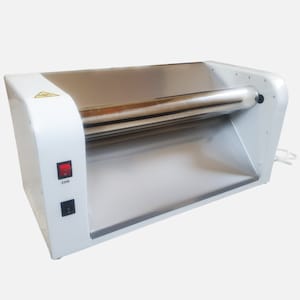 Puede incluir: Máquina eléctrica para hacer pasta de color blanco y plateado con un interruptor de encendido rojo y un cable de alimentación negro. La máquina tiene un rodillo de acero inoxidable y una etiqueta de advertencia.