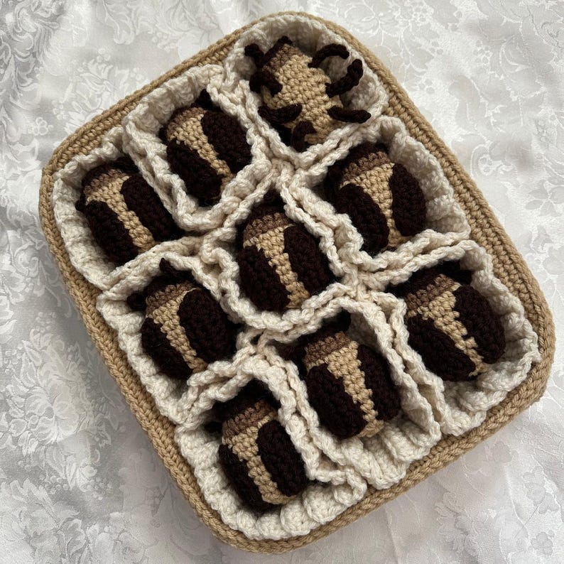 May include: A crocheted basket with a white and brown pattern holds nine crocheted brown and beige balls. The balls are arranged in a grid pattern.
