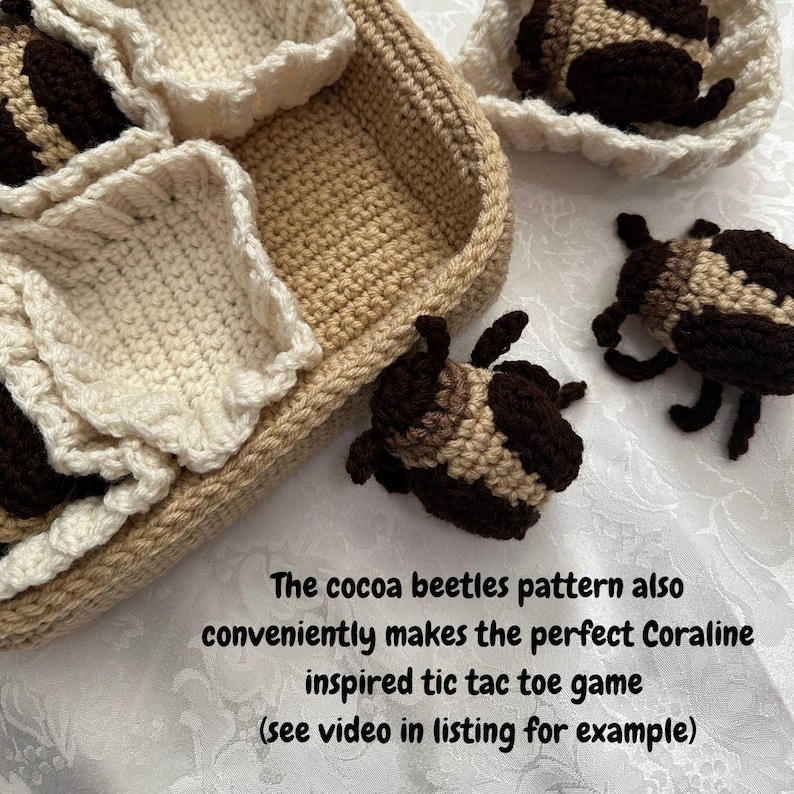 May include: Crocheted cocoa beetle toys in a brown and white basket. The beetles are brown and tan with black accents. The text "The cocoa beetles pattern also conveniently makes the perfect Coraline inspired tic tac toe game (see video in listing for example)" is below the basket.