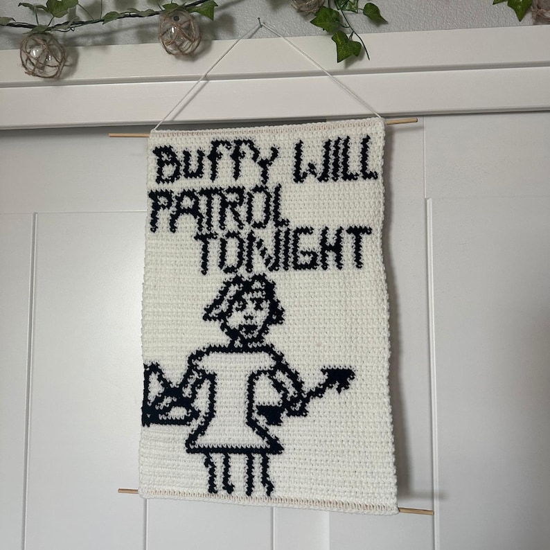 May include: White crocheted wall hanging with black text that reads "Buffy Will Patrol Tonight" and a black and white pixelated image of a person holding a stake.