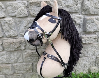 May include: A tan and white stuffed horse head with a black mane and tail. The horse is wearing a black leather bridle with a black noseband and a black throatlatch. The bridle has a silver bit and a silver buckle.