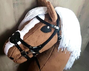 Può includere: Una testa di cavallo di peluche marrone e bianca con una briglia e redini in pelle nera. Il cavallo ha una criniera e una coda bianche.