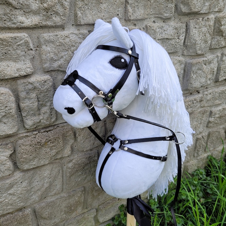 May include: White plush horse head with a black leather bridle and reins. The horse has a white mane and tail.