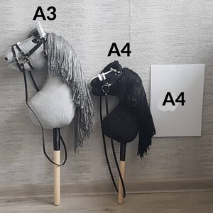 K&ouml;nnte beinhalten: Zwei Spielzeug-Schaukelpferde, eines grau und eines schwarz, mit Holzst&ouml;cken und Z&uuml;geln. Das graue Pferd hat den Text "A3" dar&uuml;ber und das schwarze Pferd den Text "A4" dar&uuml;ber. Ein wei&szlig;es Schild mit dem Text "A4" befindet sich im Hintergrund.