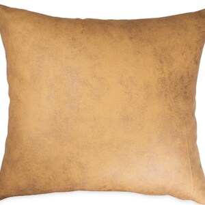 May include: A square, tan-colored pillow with a textured, distressed appearance. The pillow has a solid color and a soft, inviting look. The pillow is likely for home decor, adding a touch of warmth and style to any living space.