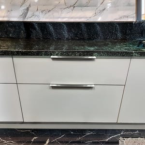 May include: A contemporary kitchen design with light grey cabinets and stainless steel handles. The countertop is black with a speckled pattern, and the backsplash is white with grey veining. A stainless steel sink is visible.