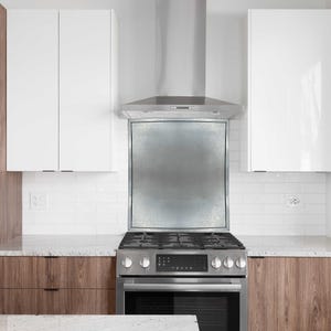 May include: Modern kitchen with white upper cabinets and wood-grain lower cabinets. A stainless steel range and hood are centered above the countertop. The backsplash is white subway tile. A stainless steel refrigerator is on the left.