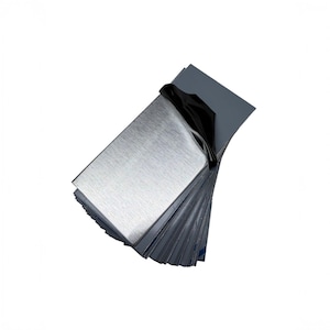 May include: A stack of rectangular metal sheets with a brushed silver finish. The top sheet is partially peeled back to reveal a smooth, black underside. The sheets are layered neatly, showing a consistent metallic texture and sharp edges.