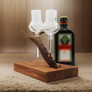 May include: A wooden stand with two clear glass shot glasses and a bottle of Jagermeister. The stand is made from a piece of antler.
