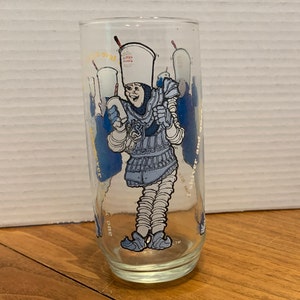 May include: A clear glass with a blue and white illustration of a cartoon character wearing a crown and holding a cup. The text "I shiver and quiver" is on the glass.