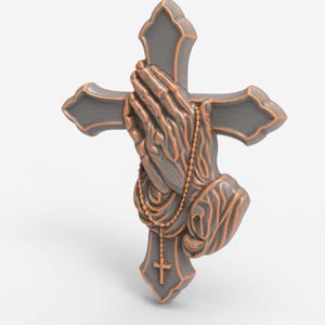 May include: A gray cross with bronze-colored praying hands and a rosary. The cross has ornate edges and a small cross at the bottom. The hands are clasped in prayer, with the rosary beads draped over them.