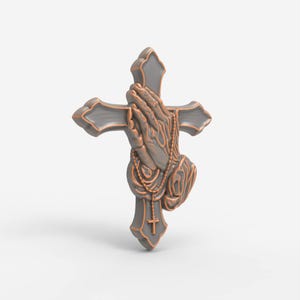 May include: A three-dimensional wall ornament featuring a grey cross with copper-colored edges. The center displays a relief sculpture of two hands pressed together in prayer, draped with a beaded rosary that includes a small cross pendant.