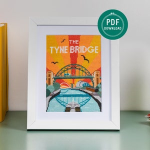 May include: A framed cross-stitch pattern of the Tyne Bridge in Newcastle upon Tyne, England. The bridge is depicted in a colourful, retro style with a yellow, orange, and blue colour scheme. The text "The Tyne Bridge" is printed above the bridge.