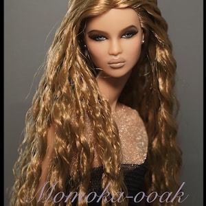 May include: A fashion doll with long, wavy, golden-brown hair, dark eye makeup, and nude-colored lips. The doll wears a black top with a shimmering gold mesh neckline. The text Momoka-ooak is printed in a cursive font at the bottom.