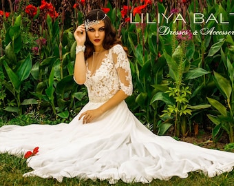 May include: A woman wearing a white lace wedding dress with a beaded crown sits in a garden with red flowers. The text "LILIYA BALTINA Dresses & Accessories" is visible in the image.