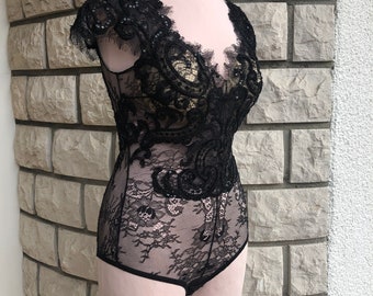 May include: Black lace bodysuit with a delicate floral pattern and beaded embellishments. The bodysuit has a V-neckline and short sleeves.