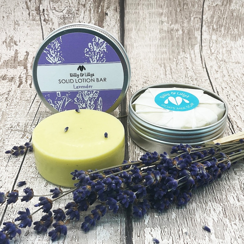 May include: A round, yellow solid lotion bar in a silver tin with a lavender floral design and the text "Billy & Lilly's SOLID LOTION BAR Lavender".