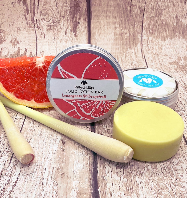 May include: A round, yellow solid lotion bar in a silver tin with a red grapefruit and green lemongrass design. The tin has the text "Billy & Lilly's Solid Lotion Bar Lemongrass & Grapefruit". A grapefruit slice and two lemongrass stalks are in the background.
