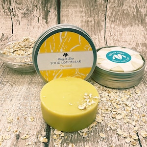 May include: A round, yellow, solid lotion bar in a silver tin with the text "Billy & Lilly's SOLID LOTION BAR Oatmeal" on the label. The bar is surrounded by rolled oats.
