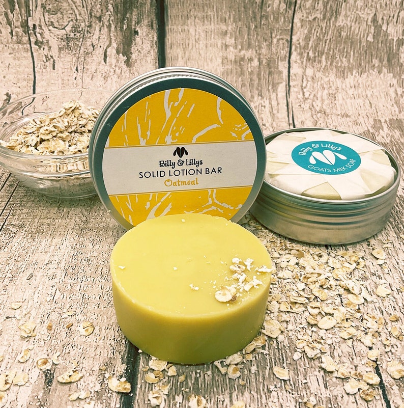 May include: A round, yellow, solid lotion bar in a silver tin with the text "Billy & Lilly's SOLID LOTION BAR Oatmeal" on the label. The bar is surrounded by rolled oats.