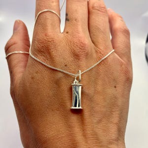 Single sterling silver breathing pendant held in a hand to show its size.