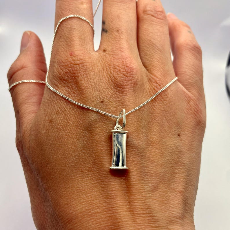 Single sterling silver breathing pendant held in a hand to show its size.