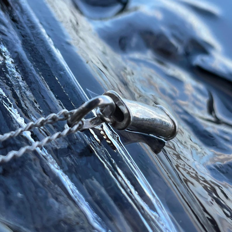 Sterling silver breathing pendant photographed against blue water.