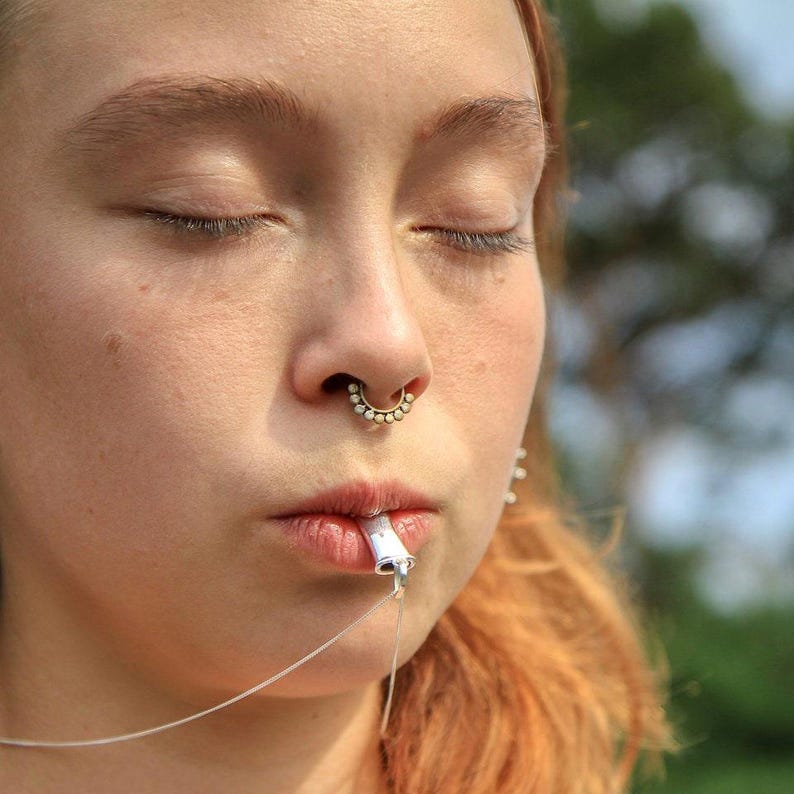 Person with eyes closed using the sterling silver breathing necklace outdoors.