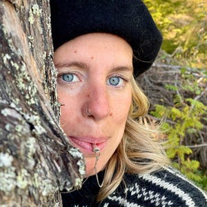 Person in a beret using the sterling silver breathing pendant beside a tree.