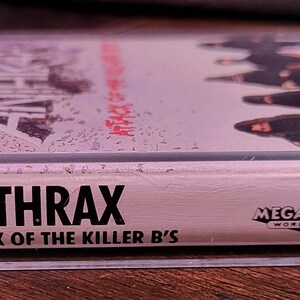 May include: A clear cassette tape featuring the band Anthrax's album "Attack of the Killer B's." The album cover shows the band members and the text "Anthrax" in bold letters. The cassette case has a rainbow-colored Island Records logo.