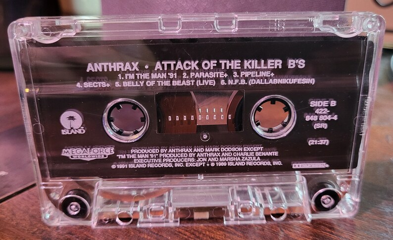 May include: Clear cassette tape of Anthrax's "Attack of the Killer B's" album. The cassette features the album title, tracklist, and Island Records logo. Side B details include the catalog number and a total running time of 21:37.