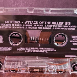 May include: Clear cassette tape with the album title "Attack of the Killer B's" by Anthrax. The black label features song titles and the Island Records logo. The tape is in a clear plastic case.