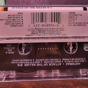May include: A clear cassette tape case with the album title "Attack of the Killer B's" and the band name Anthrax. The cassette tape has a black label with song titles and a barcode. The Island Records logo is visible.