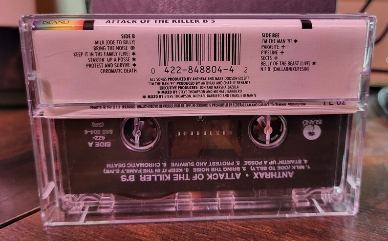 May include: A clear cassette tape case with the album title "Attack of the Killer B's" and the band name Anthrax. The cassette tape has a black label with song titles and a barcode. The Island Records logo is visible.
