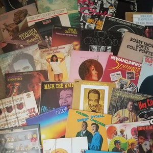 May include: A collection of vintage vinyl records, featuring album covers with various artists and titles. The covers display a range of colors and designs, showcasing portraits, text, and graphic elements. The records are stacked together, creating a nostalgic display.