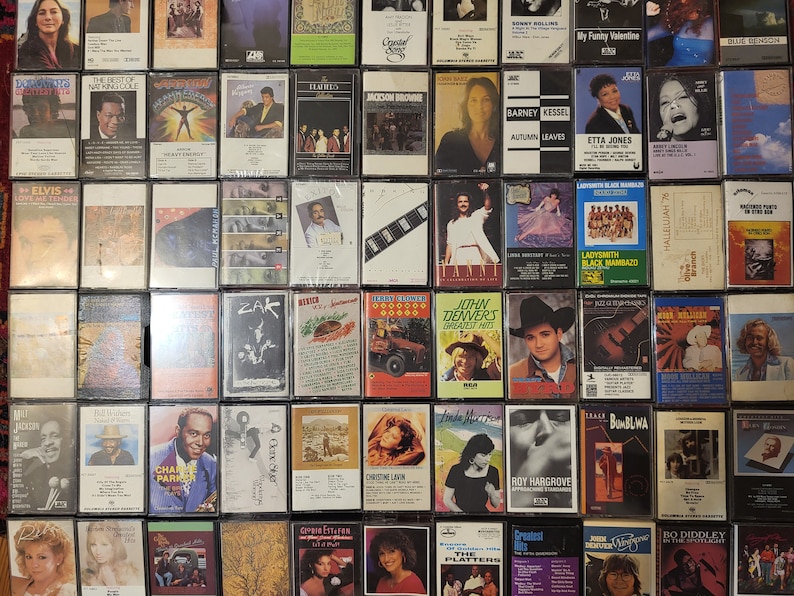 May include: A selection of vintage cassette tapes, displaying a variety of music albums and artists. The tapes are arranged in a grid, with diverse album covers and designs. Some tapes feature text such as "Elvis", "John Denver", and "Etta Jones".