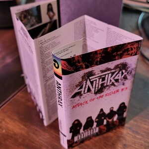 May include: Anthrax "Attack of the Killer B's" cassette tape. The cover features the band's logo and album title in red and white. The cassette case is open, revealing the interior with song lyrics and images.