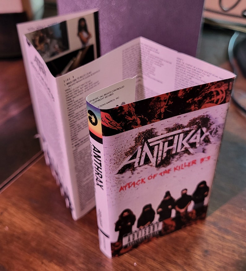 May include: Anthrax "Attack of the Killer B's" cassette tape. The cover features the band's logo and album title in red and white. The cassette case is open, revealing the interior with song lyrics and images.