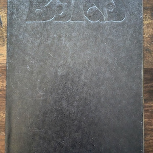 May include: A dark gray book with the embossed text "THE CURE" on the cover. The book has a textured, worn appearance, suggesting it is vintage or has been well-used. The background is a wooden surface.