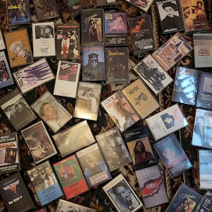 May include: A selection of vintage cassette tapes, displaying album artwork with text and images. The tapes are arranged on a patterned surface, representing a range of music genres and artists from different periods.